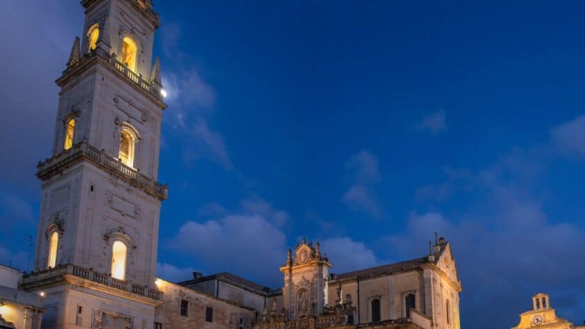 Imponente campanile illuminato a Lecce durante il crepuscolo, con il cielo blu intenso sullo sfondo.