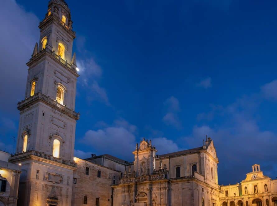 Imponente campanile illuminato a Lecce durante il crepuscolo, con il cielo blu intenso sullo sfondo.