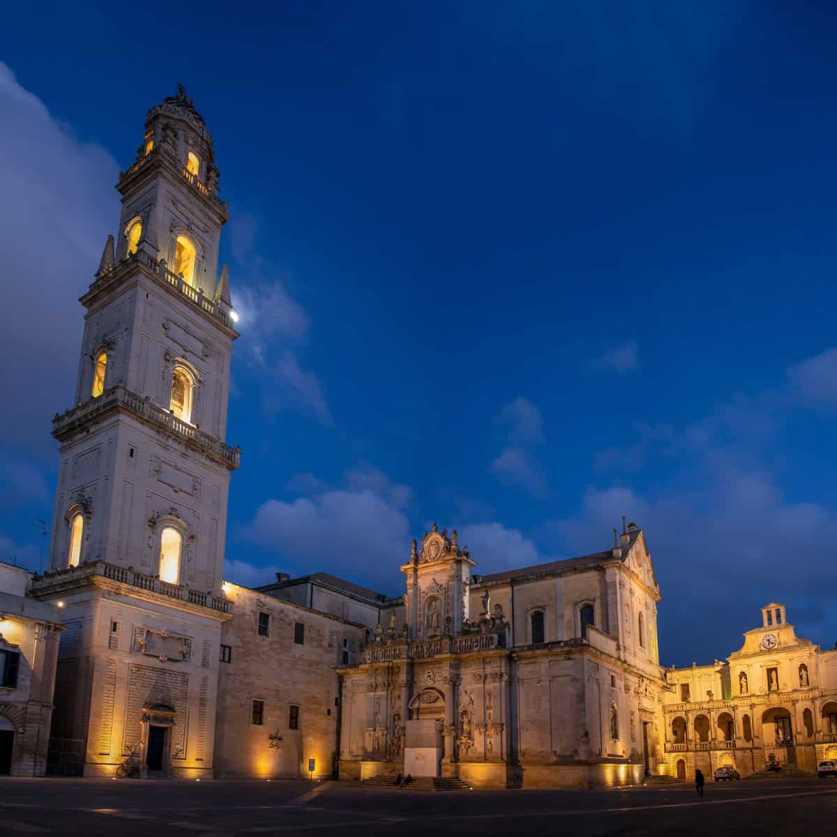 Imponente campanile illuminato a Lecce durante il crepuscolo, con il cielo blu intenso sullo sfondo.