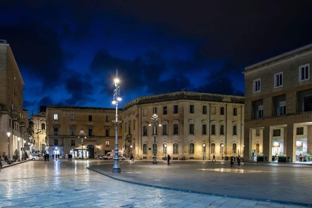 Piazza di Lecce illuminata di sera con edifici storici e cielo notturno.