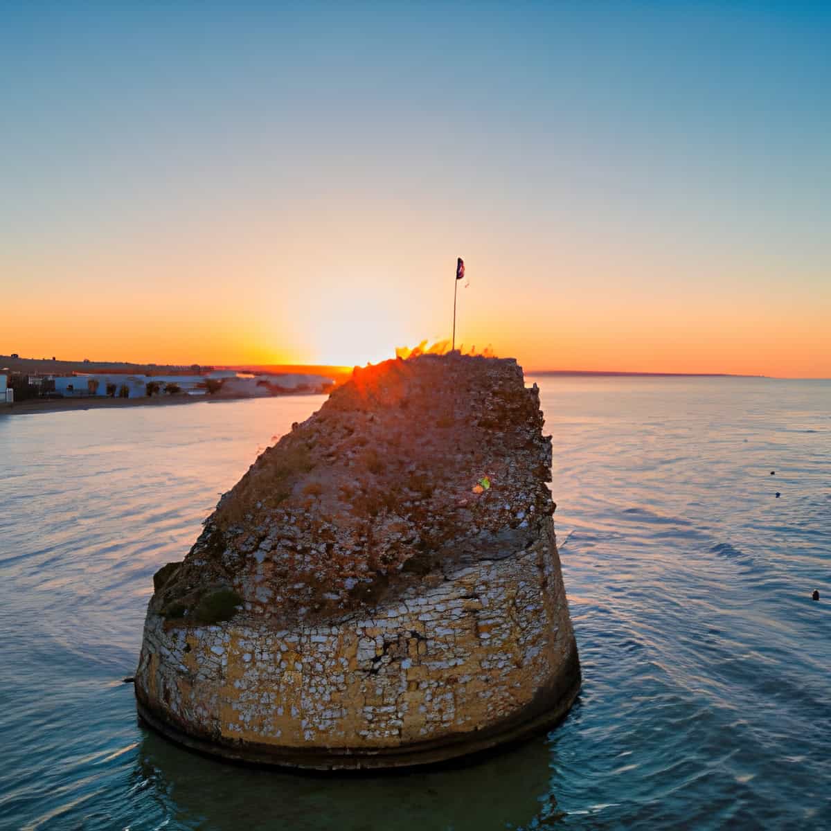 Torre di Puglia al tramonto con vista sul mare e bandiera italiana.