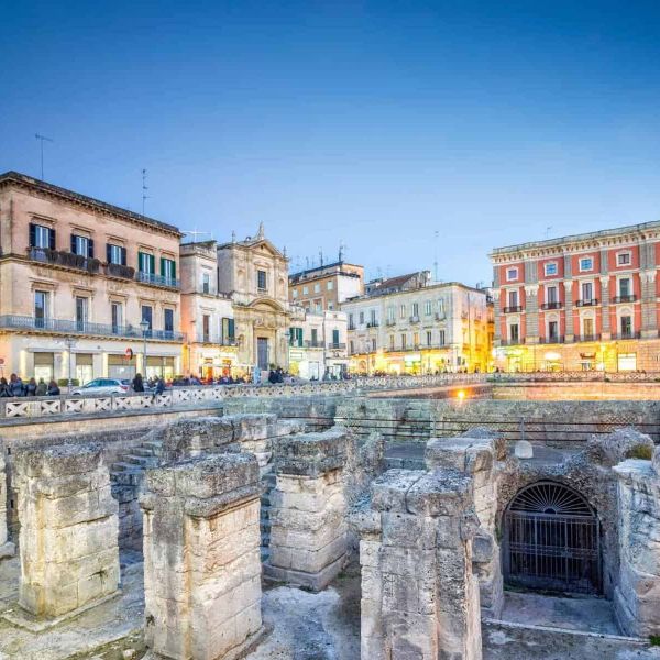 Architettura storica e scavi archeologici a Palermo al tramonto, con edifici illuminati e cielo sereno.