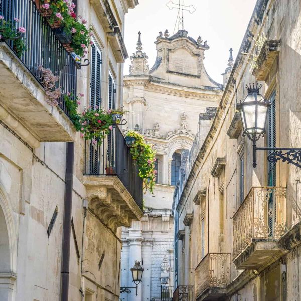 Vicolo pittoresco con balconi fioriti e lampioni in stile in una città italiana storica.